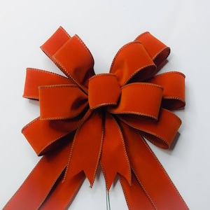 May include: A large, burnt orange velvet bow with wired tails. The bow is tied with a single loop and has a slightly frayed edge.