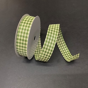 May include: A spool of green and white checkered ribbon. The ribbon is unspooled, with a portion of it curving away from the spool. The ribbon is made of fabric and is suitable for crafts and gift wrapping.