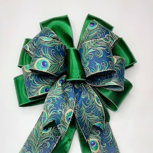 May include: A green and blue peacock feather patterned bow with a green satin ribbon. The bow is tied in a large, decorative knot.