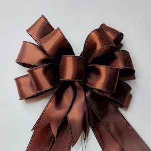 May include: A large brown satin bow with a center loop and long tails. The bow is tied with a single knot and has a smooth, shiny finish.