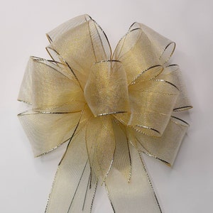 May include: A gold sheer ribbon bow with a gold wired edge. The bow is tied in a classic shape with two long tails.