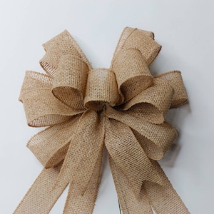 May include: A large, brown burlap bow with a rustic, farmhouse style. The bow is tied with a long tail and is perfect for adding a touch of country charm to any decor.