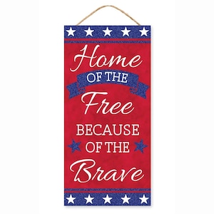 May include: Red wooden sign with a white background and blue glitter stars. The sign says "Home of the Free Because of the Brave".