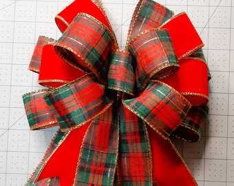 May include: A red and green plaid ribbon bow with gold trim. The bow is tied with a red velvet ribbon.