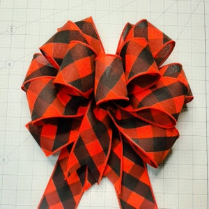 May include: A large red and black plaid bow with a wired edge. The bow is made of ribbon and is tied in a classic bow shape.