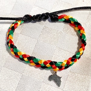 Peut inclure: Un bracelet tressé avec des fils rouges, jaunes, verts et noirs. Le bracelet a un charme argenté en forme du continent africain.
