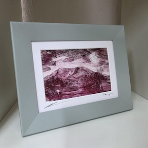 May include: A framed art print featuring a dark maroon and white abstract landscape illustration with visible etched lines. The artwork is set within a white mat and a wide, smooth, light gray frame with angled edges and a signature in the corner.