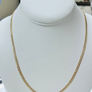 May include: A gold chain necklace with a curb link design. The chain is on a white display stand.
