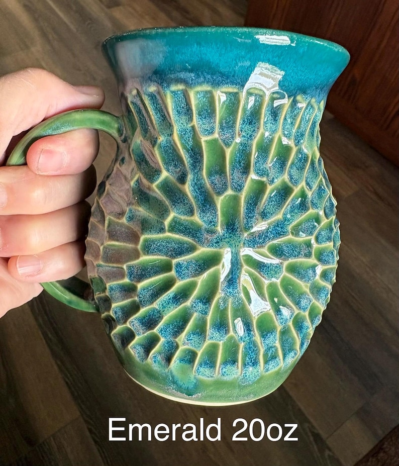 May include: A ceramic mug with a 20oz capacity, featuring a textured, honeycomb-like pattern on the exterior. The glaze transitions from a deep emerald green at the base to a vibrant teal at the rim. The mug includes a curved handle on the side.