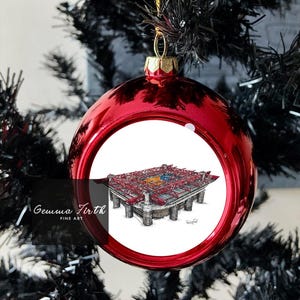 Könnte beinhalten: Eine glänzende rote Weihnachtskugel mit einer detaillierten architektonischen Zeichnung im Inneren. Die Kugel hängt an einem goldenen Faden an einem schwarzen Weihnachtsbaum. Die Zeichnung zeigt ein Gebäude mit roten und grauen Elementen.