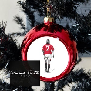 May include: A red bauble with a gold cap and string, hanging on a black Christmas tree. The bauble features a drawing of a footballer in a red jersey with the number 7. The text "Gemma Firth FINE ART" is on the bottom.