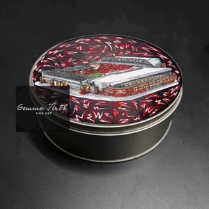 Puede incluir: Una lata redonda plateada con una ilustración detallada de un estadio en la tapa. El estadio está representado en rojo, blanco y gris, sobre un fondo negro con diseños abstractos rojos. La lata tiene el texto "Gemma Firth Fine Art".