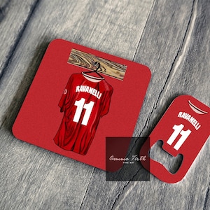 Könnte beinhalten: Rotes und weißes Fußballtrikot mit dem Namen "Ravanelli" und der Nummer "11" auf dem Rücken. Das Trikot hängt an einem Holzaufhänger. Das Trikot befindet sich auf einem roten Untersetzer mit einem Flaschenöffner.