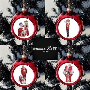 Può includere: Quattro palline di Natale rosse con illustrazioni di calciatori con maglie rosse. Le palline sono appese a un albero di Natale nero. Le palline hanno una finitura lucida. Il testo "Gemma Firth FINE ART" è al centro.