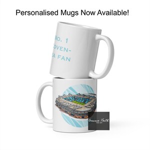 Può includere: Due tazze di ceramica bianca impilate. La tazza superiore presenta il testo "No. 1 OVEN-SEA FAN" in azzurro. La tazza inferiore presenta un'illustrazione dello stadio con sfondo blu e bianco.