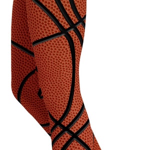 May include: Leggings with a basketball design. The leggings are orange with black lines, mimicking the look of a basketball. The leggings are form-fitting and cover the legs.