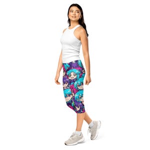 Może przedstawiać: Legginsy capri z żywym wzorem twarzy postaci w stylu anime w odcieniach niebieskiego, fioletowego i różowego. Legginsy są noszone z białym topem na ramiączkach i szarymi trampkami. Ogólny styl jest swobodny i kolorowy.