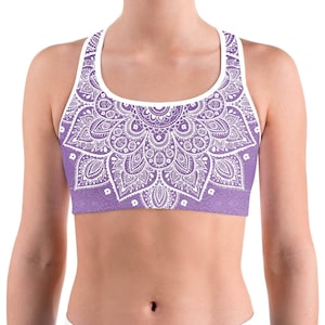 May include: A lavender sports bra featuring a white mandala pattern. The bra has a scoop neck and a racerback design. The detailed floral design covers the front of the bra, with white trim around the neckline and armholes.