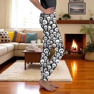 Puede incluir: Leggings negros y blancos con un patrón repetido de caras de calaveras estilizadas. Los leggings son ajustados y llegan a los tobillos. Las calaveras son blancas con contornos y detalles negros, sobre un fondo negro.
