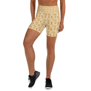 May include: High-waisted yoga shorts with a repeating pattern of yellow and gold botanical elements on a white background. The shorts are worn with black athletic shoes. The shorts are made of a stretchy, comfortable material.