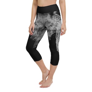 May include: Black and white capri leggings with an angel wing design on the right leg. The leggings have a high waistband and a smoky, cloud-like pattern on the front. The design is printed on a black background.