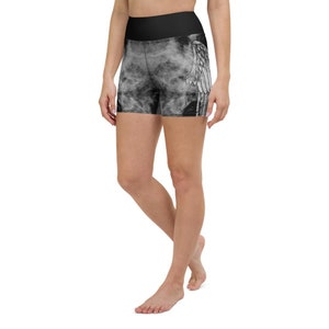 May include: Black yoga shorts with a high waistband. The shorts feature a white wing design on the side and a smoky, cloud-like pattern. The shorts are made of a stretchy material.