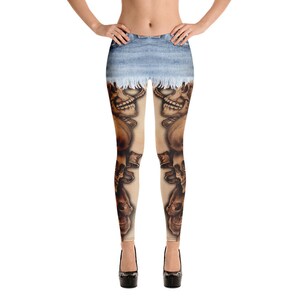 Op de afbeelding: Legging met een print van een lichtblauwe spijkerrok met een gerafelde zoom bij de taille. De benen tonen een gedetailleerde grafische print van meerdere bruine en beige menselijke schedels die verticaal tot aan de enkels zijn gestapeld.
