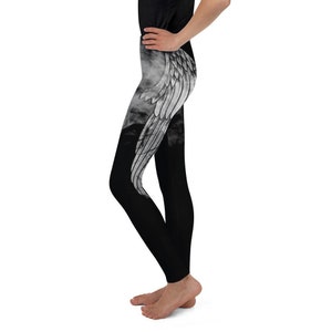 May include: Black leggings featuring a large, detailed white wing graphic printed on the upper thigh and hip area. The design includes soft, smoky grey shading around the wing, contrasting against the solid black fabric of the rest of the garment.