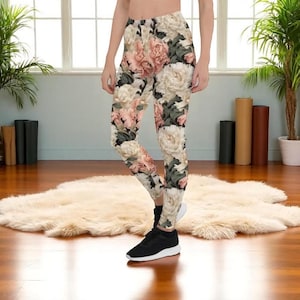 Może przedstawiać: Legginsy w kwiaty z wzorem dużych, jasnoróżowych i białych piwonii na beżowym tle. Legginsy są dopasowane i wykonane z elastycznego materiału. Projekt zawiera zielone liście, tworząc motyw botaniczny. Noszone z czarnymi trampkami.