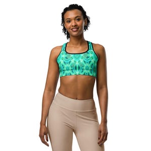 May include: A teal and green sports bra with a black trim and a floral pattern. The bra is worn by a person wearing beige leggings. The sports bra is designed for athletic activities.