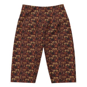 Può includere: Pantaloni da yoga marroni con un motivo ripetuto di corna di ariete, lune crescenti e forme a diamante nei toni dell'oro, dell'arancione e del nero. I pantaloni sono realizzati in un materiale morbido ed elastico.