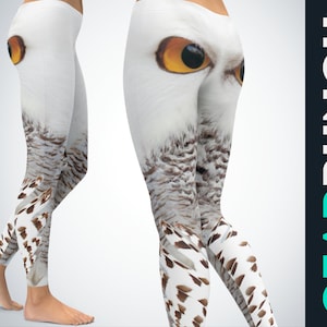 Könnte beinhalten: Weiße Leggings mit einem hochauflösenden Grafikdruck eines Schnee-Eulengesichts. Das Design zeigt große, stechende bernsteinfarbene Augen im Hüftbereich, die in ein weiß-braunes, geflecktes Feder-Muster entlang der Beine bis zu den Knöcheln übergehen.