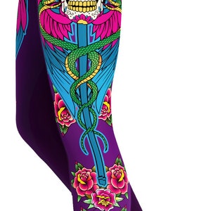 Peut inclure: Legging violet avec un imprimé graphique vibrant représentant un crâne en sucre orné de roses roses, d'une épée bleue et d'un serpent vert. Le motif comprend des grappes de roses roses supplémentaires en haut et en bas sur fond violet.