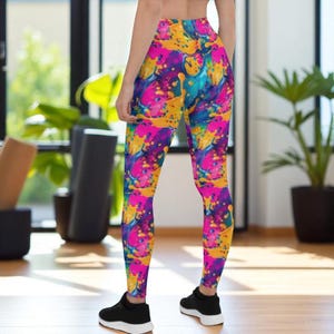 Może przedstawiać: Legginsy z wysokim stanem z żywym, abstrakcyjnym wzorem plam farby w odcieniach różu, żółci, niebieskiego i fioletu. Legginsy są noszone z czarnymi butami sportowymi. Legginsy są wykonane z wygodnego, elastycznego materiału.