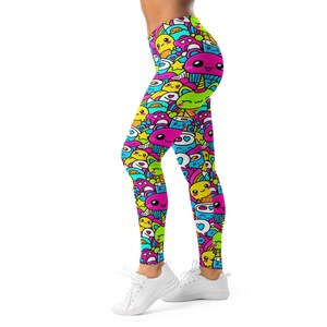May include: Brightly coloured leggings with a pattern of cartoon characters in pink, yellow, blue, and green. The leggings are form-fitting and made of a stretchy material. The design includes cupcakes, stars, and other playful elements.