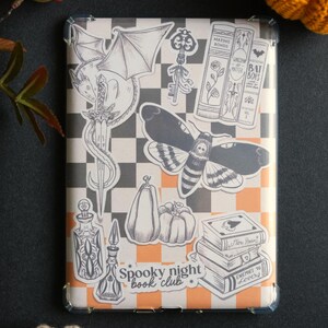 Puede incluir: Una funda decorativa con un patrón de tablero de ajedrez en blanco y negro y bordes naranjas. La funda está adornada con ilustraciones de un dragón, una polilla, libros, llaves, calabazas y botellas de pociones. También se ve el texto "Spooky night book club".