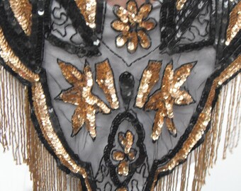 May include: A black and gold sequined shoulder wrap with fringe. The wrap features a floral design with gold sequins and black trim. The fringe is a matching gold color. The wrap is likely vintage and suitable for formal events.