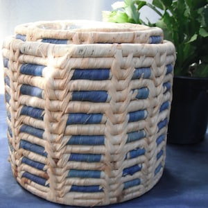 May include: A woven basket with a blue and white pattern. The basket is made of natural materials and has a round shape.