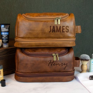 May include: Two brown leather travel bags with zipper closures. The top bag has the name "JAMES" embossed on the front. The bottom bag has the name "Henry" embossed on the front.
