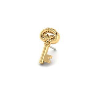 May include: A gold-colored key earring with an ornate design. The key has a decorative top and a straight shaft with a small, rectangular keyhole.