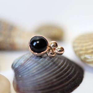 May include: A black onyx gemstone set in a rose gold cluster of beads. The cluster is made of three small beads.