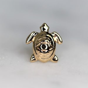 May include: A gold-coloured turtle charm with a detailed design. The turtle is facing forward with its head raised and its legs outstretched.
