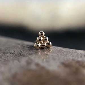 May include: A gold triangle-shaped stud earring with a cluster of small, round beads.