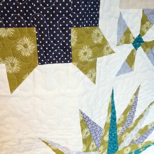 May include: A close-up of a quilt with a patchwork design. The quilt is made of different fabrics in shades of green, blue, and white. The quilt is quilted with a simple stitch pattern.