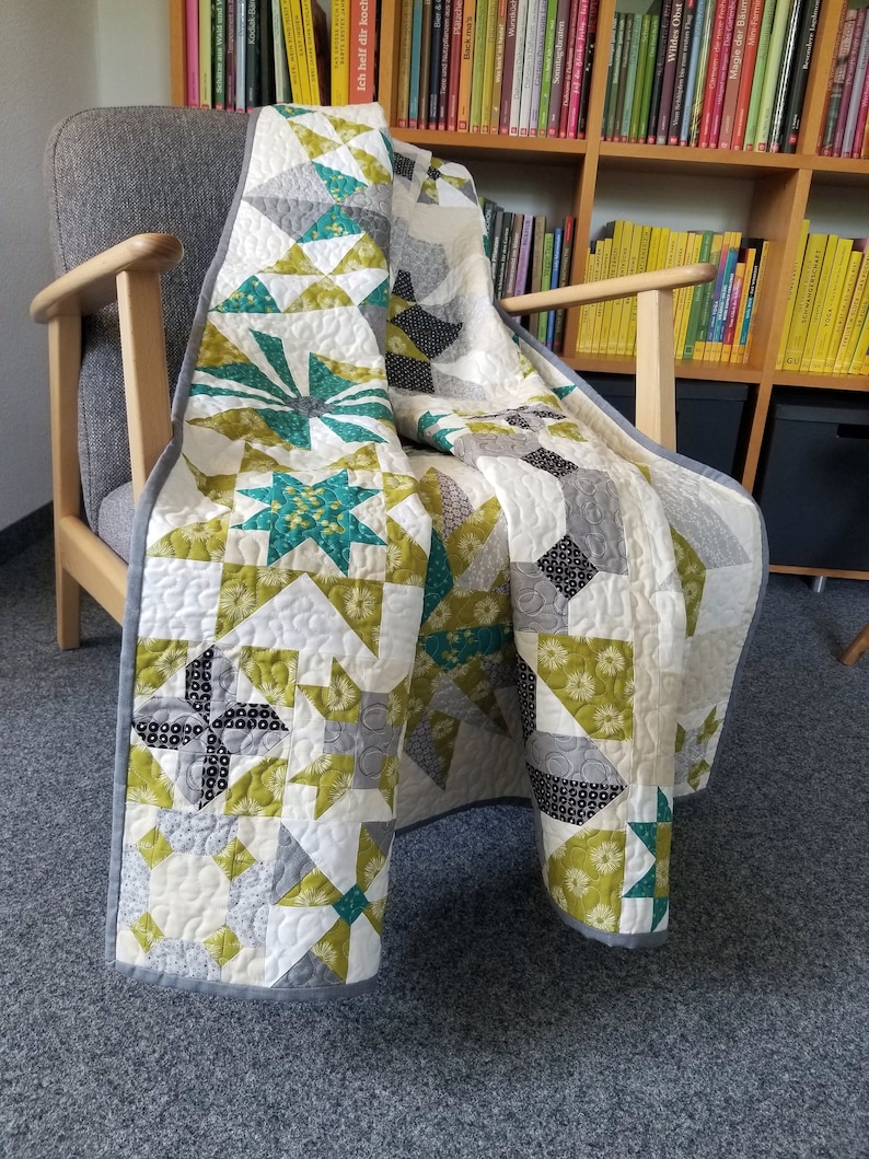 May include: A patchwork quilt with a variety of geometric patterns in shades of green, gray, and white. The quilt is folded and draped over a wooden armchair.