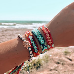 Puede incluir: Tres pulseras de amistad coloridas con patrones geométricos, una pulsera de cuentas blancas con un dije de tortuga y una borla multicolor.