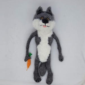 Peut inclure: Poupée loup au crochet faite à la main, grise, blanche et noire, tenant une carotte orange avec des feuilles vertes. Le loup a une poitrine blanche, un nez noir et une langue rose. Un jouet doux.