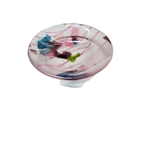 May include: A decorative glass dish with a rounded shape and a light pink hue. The dish features abstract designs in shades of blue, green, and purple, with thin, swirling lines. The base is white. This unique piece is ideal for home decor.