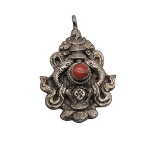 Puede incluir: Colgante de plata con un diseño ornamentado. Presenta dos figuras serpentinas que flanquean una piedra roja redonda central. El colgante tiene una parte superior detallada y en capas y una base floral, con intrincados patrones.