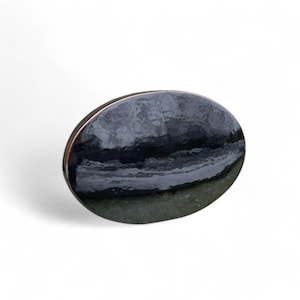 May include: A black oval ceramic dish with a slightly raised rim and a glossy finish. The dish has a subtle texture and a slight curve in the center.